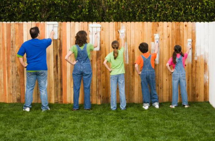 Famille qui peint une clôture en bois dans un jardin